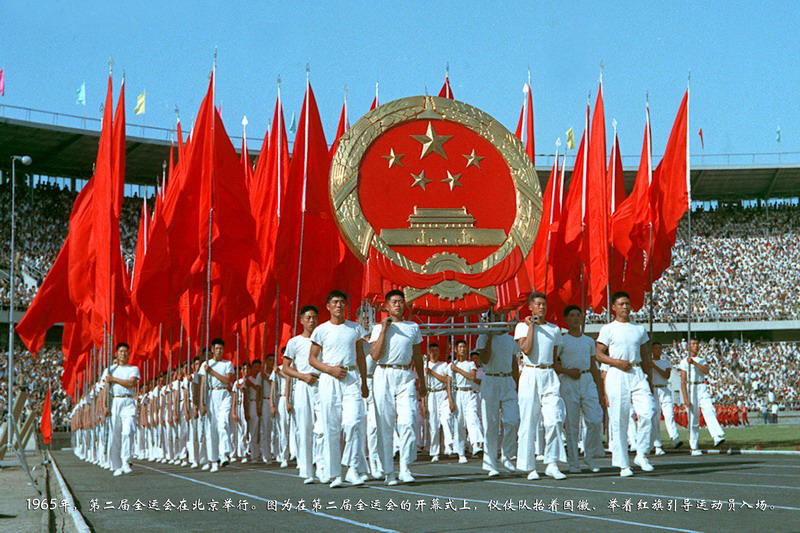 1965年，第二届全运会在北京举行。图为9月11日，在开幕式上，仪仗队抬着国徽、举着红旗引导运动员入场。