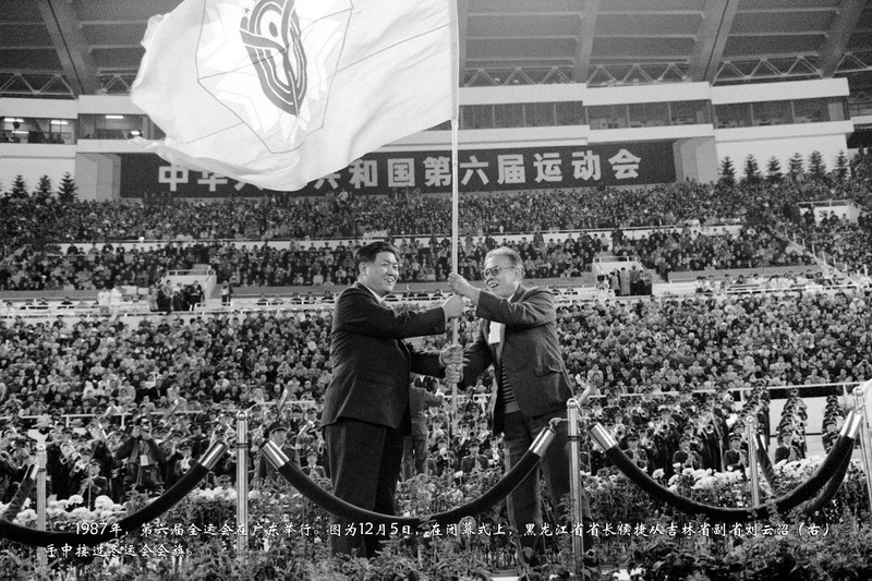 1987年，第六届全运会在广东举行。图为12月5日，在闭幕式上，黑龙江省省长侯捷从吉林省副省刘云沼（右）手中接过冬运会会旗。